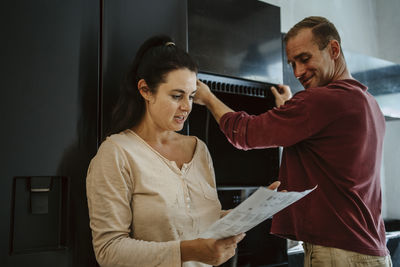 Couple discussing over document while fixing cabinet in kitchen during home renovation