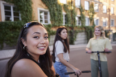 Young female friends spending time together outdoors riding electric scooters