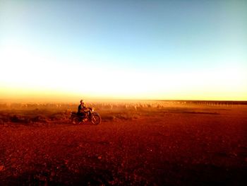 Man riding motorcycle on field against sky during sunset