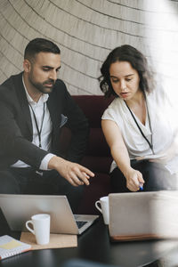 Male and female professionals discussing over laptop while sitting on sofa during networking event