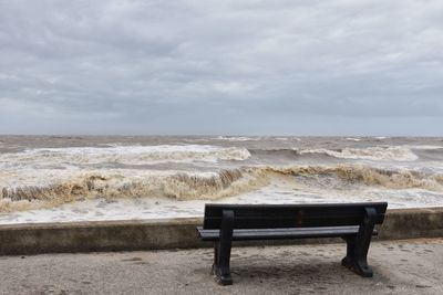 Bench on beach against sky