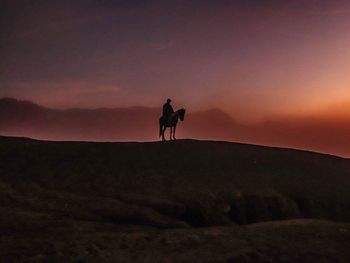 Silhouette man walking on mountain against sky during sunset