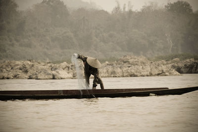 Fisherman pulling net while standing on boat in river