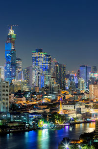 Illuminated modern buildings in city against clear sky at night