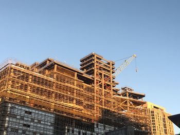 Low angle view of crane by building against clear blue sky