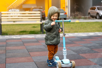 Full length of boy playing with push scooter on road