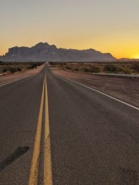 Empty road along landscape at sunset