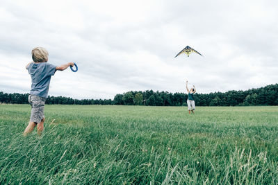 Rear view of boy standing on field against sky