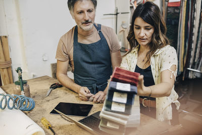 Female upholstery worker explaining male colleague over fabric swatch in workshop