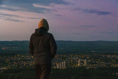 Rear view of man looking at cityscape against sky during sunset