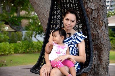 Portrait of mother with cute daughter sitting on hammock in park