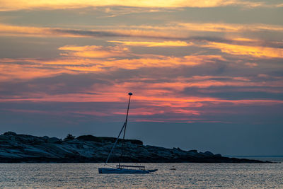 Isolated sailboat as the sun sets beyond clouds in the distance.
