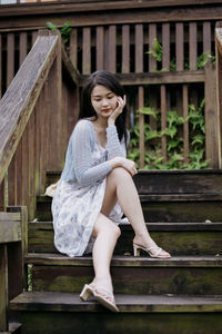 Young woman sitting on wooden wall