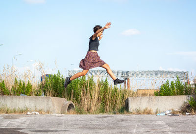 Full length of young woman jumping against sky