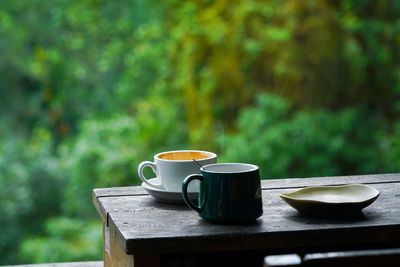 Close-up of coffee cups on wooden table against window