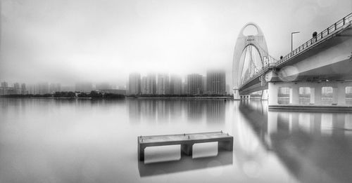 Low angle view of liede bridge over river against sky in city during foggy weather