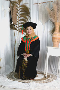 Portrait of woman wearing graduation gown sitting at home