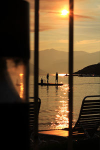 Silhouette people on diving platform in sea seen through widow during sunset