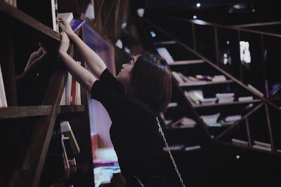 Side view of woman removing book from bookshelf in library