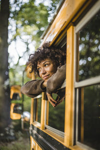 Thoughtful young woman looking through caravan window during camping in forest