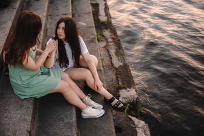 Cute lesbian couple talking while sitting on steps by river in city