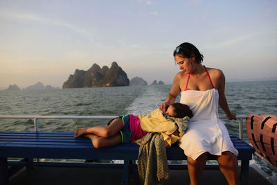 Mother looking at daughter sleeping on lap while traveling in boat