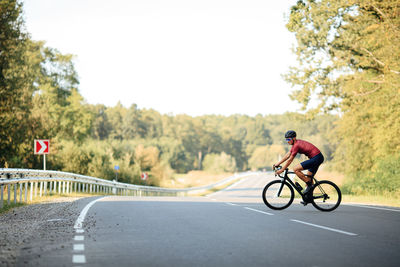 Handsome cyclist in activewear racing on paved road during morning time. 