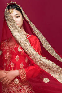 Portrait of beautiful young bride standing against red background