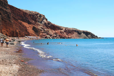 People at beach against clear blue sky