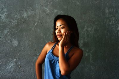 Beautiful young woman with hand on cheek standing against wall