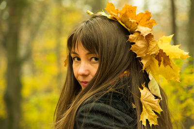 Portrait of smiling mid adult woman with autumn leaves on head at park