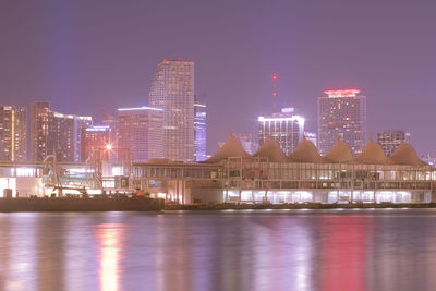 Illuminated buildings by river against sky at night