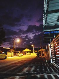 Illuminated street amidst buildings against sky at night