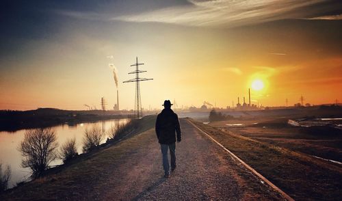 Rear view of man walking on footpath against sky during sunset