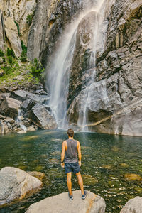 Young man standing on boulder, observing yosemite falls.