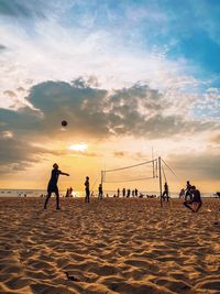 People playing on beach against sky during sunset