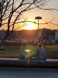 Rear view of people sitting at park during sunset