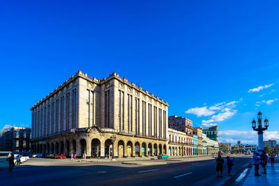 People on street by building against blue sky