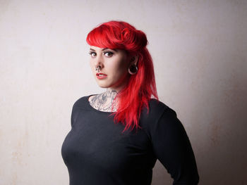 Portrait of young woman with redhead standing against wall