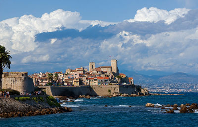 Buildings at waterfront against cloudy sky