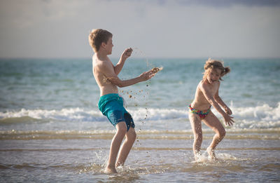 Full length of shirtless boy with girl playing at beach