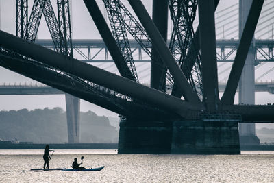People on paddleboarding by bridge at river 