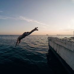 Shirtless man diving into sea against sky