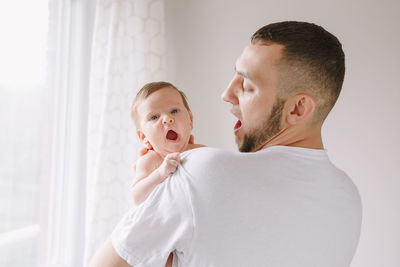 Father carrying cute baby girl yawning at home