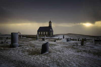 Snow covered graveyard against church during sunset