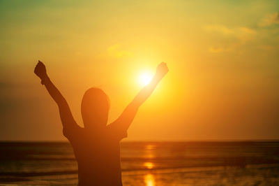 Silhouette woman with arms raised against sky during sunset