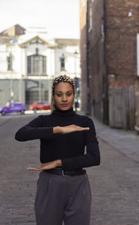 Portrait of woman gesturing while standing on footpath against buildings