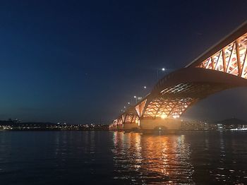 Illuminated bridge over river against sky at night