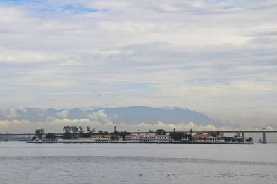 Buildings in front of sea against cloudy sky