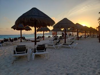 Lounge chairs and parasols on beach against sky during sunset